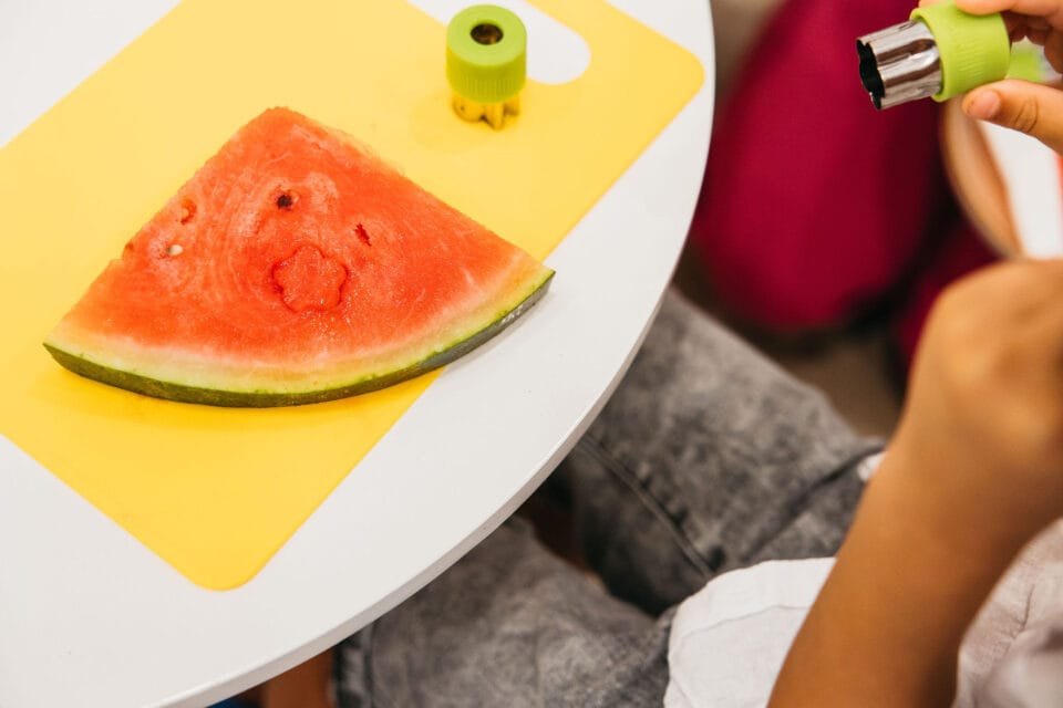 A child cutting a watermelon with a cookie cutter